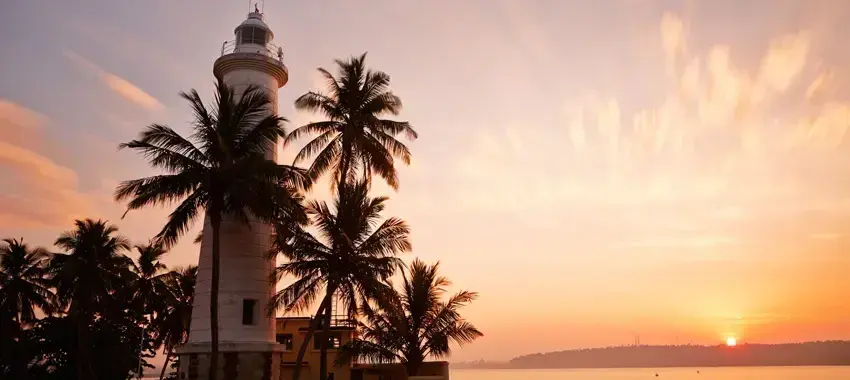 The Galle lighthouse at sunset, framed by coconut palms. [TODO: ta]